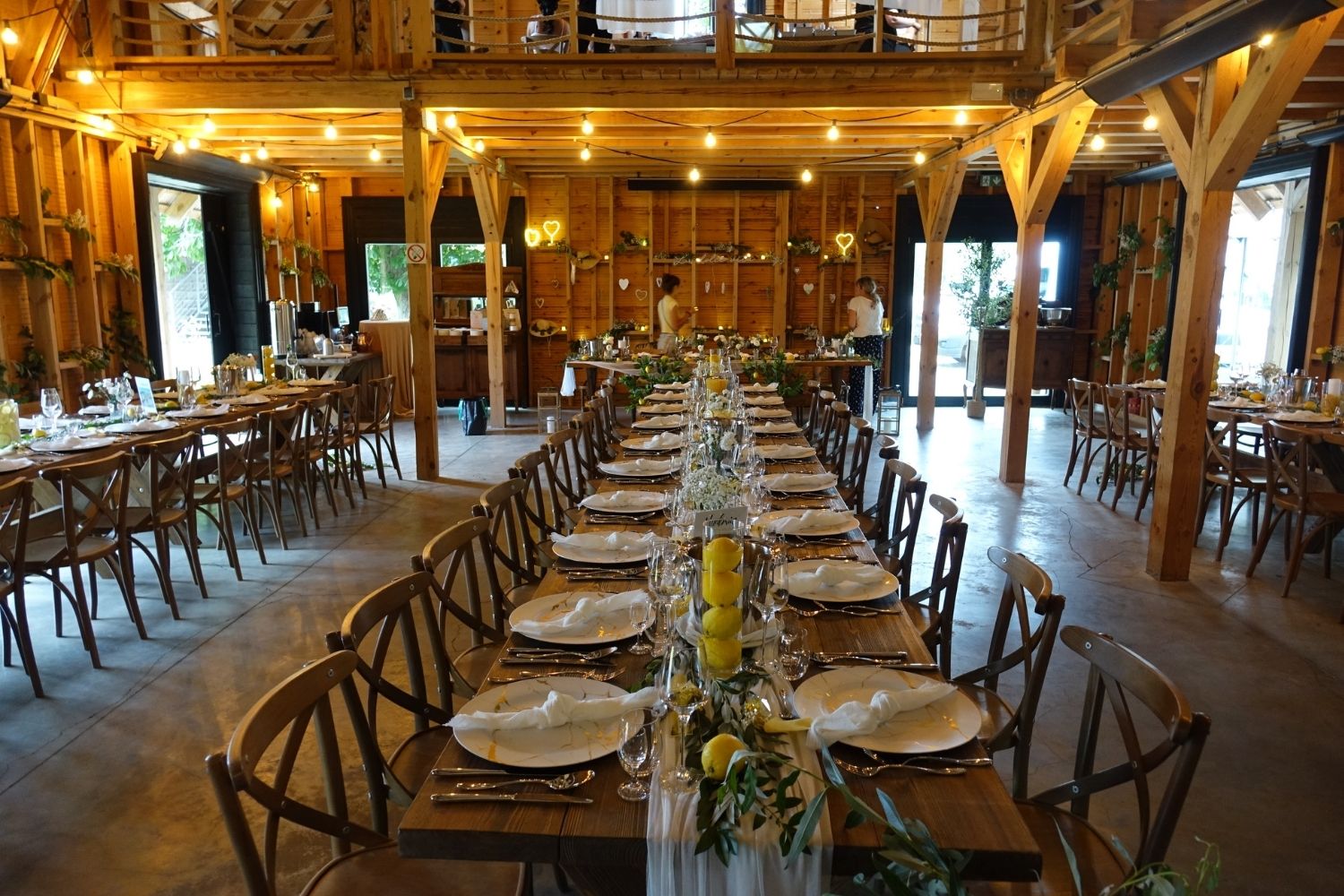 Długi, drewniany stół weselny w stylu rustykalnym, udekorowany cytrynami i zielenią, w sali o wyglądzie stodoły.