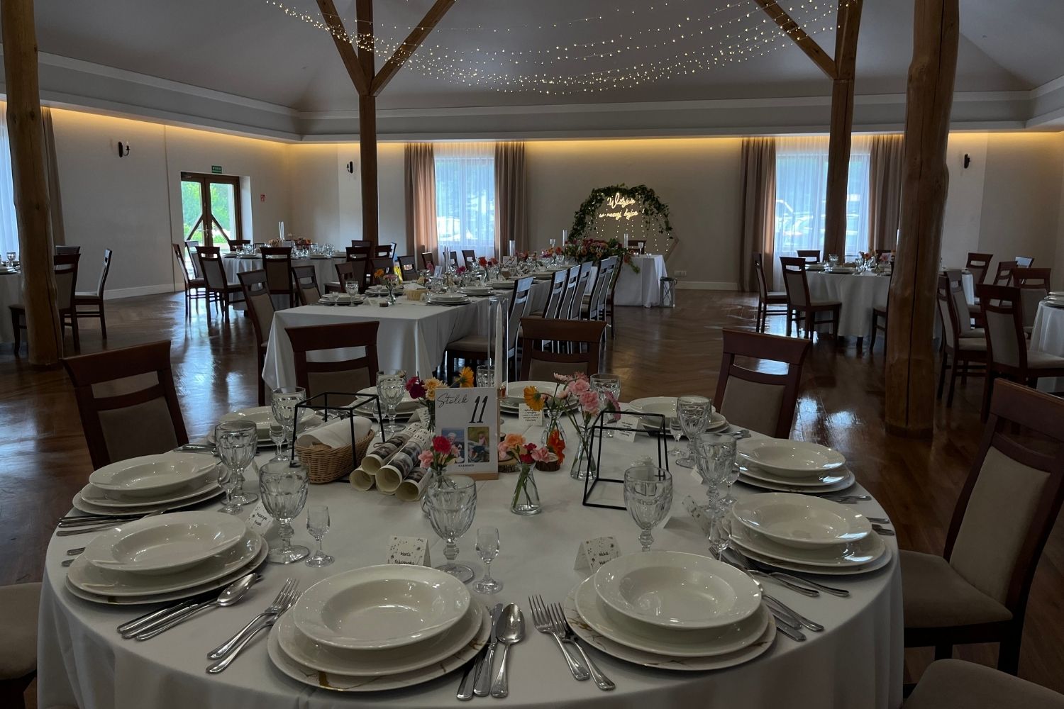 Okrągły stół weselny dla gości, w tle widoczny stół prezydialny.