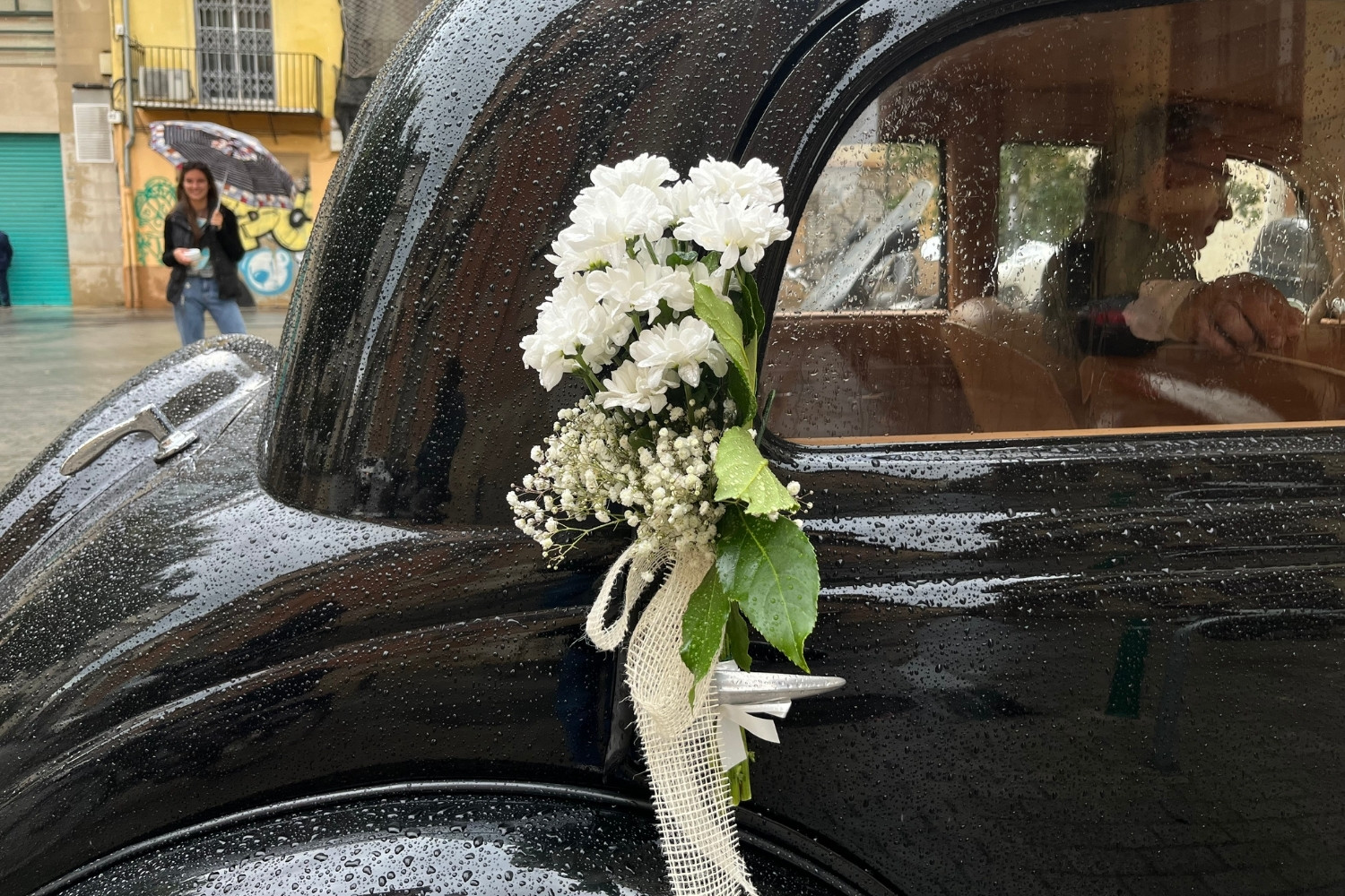 Dekoracja ślubna samochodu, bukiet z białych kwiatów i gipsówki przywiązany do klamki czarnego auta retro.